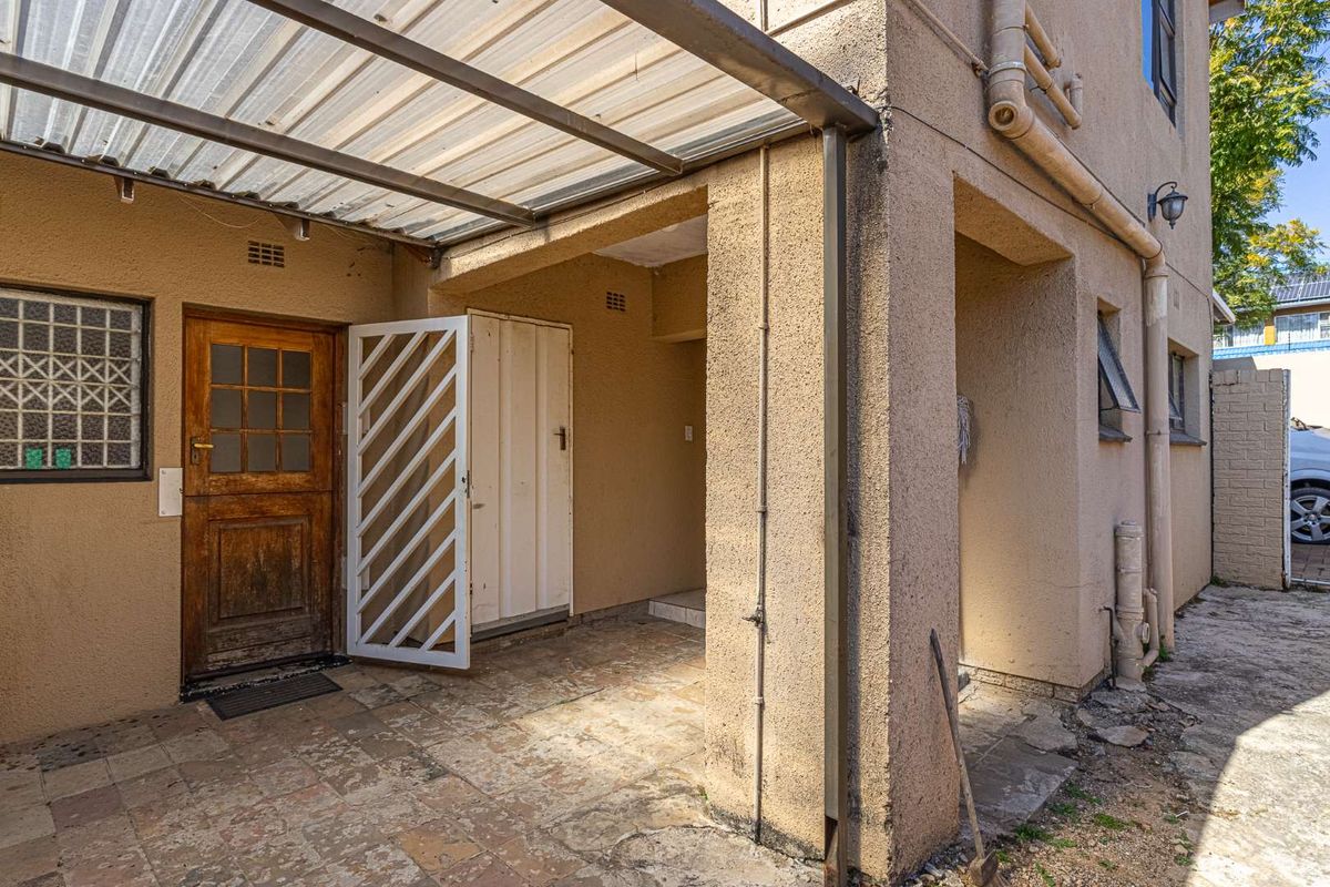 Rear exterior area featuring a paved patio, covered walkway, security gate, and timber door access to the property.