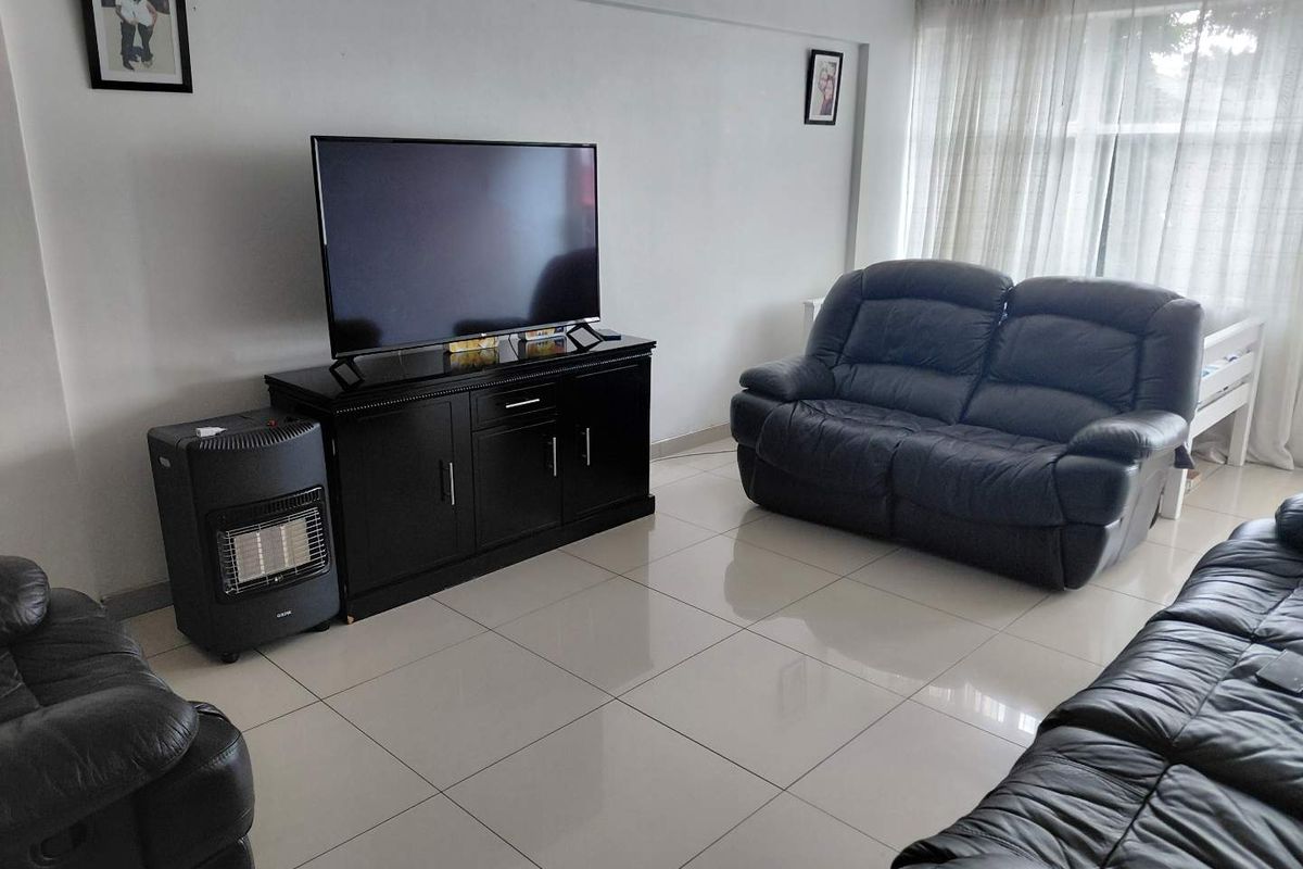 A bright living room featuring neutral tiled flooring and large windows with sheer curtains, providing a clean and functional space.