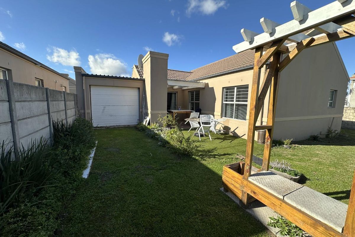 Rear exterior view of the townhouse featuring a private garden, lawn, garage access, and a wooden pergola structure.