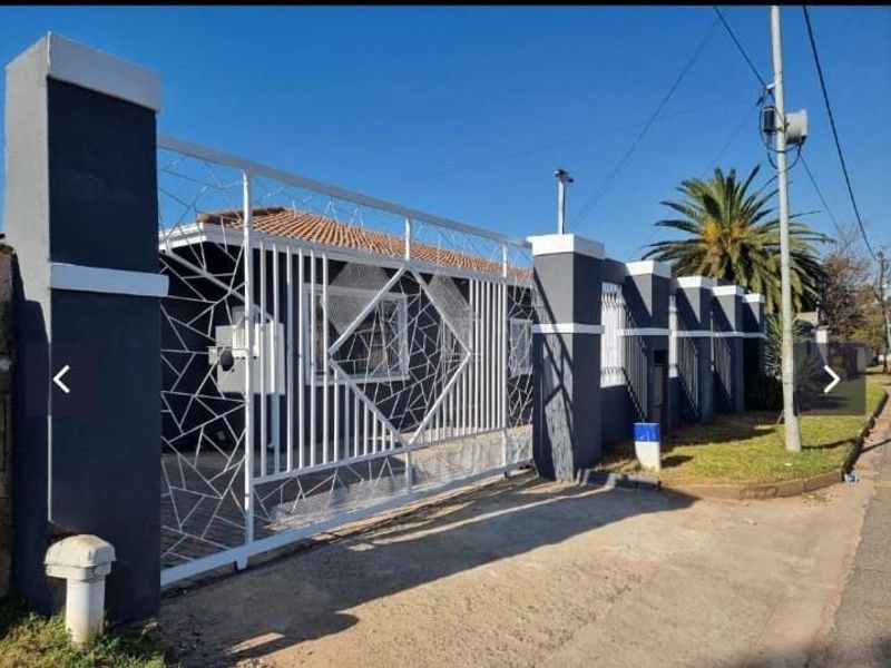 Front view of the property featuring a modern white metal security gate and a well-maintained masonry boundary wall with a tiled roof.