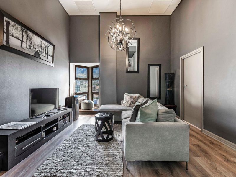A modern living room featuring high ceilings, laminate flooring, and a bay window with city views, creating a bright and contemporary atmosphere.