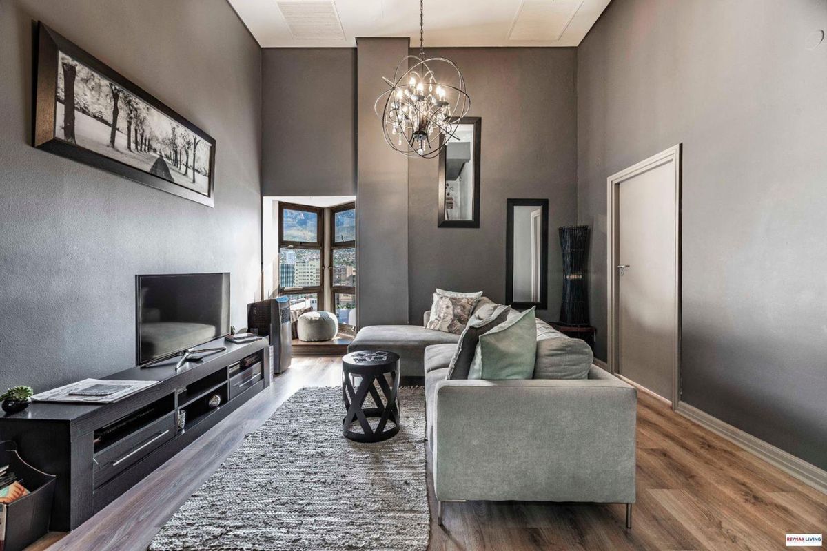 A modern living room featuring high ceilings, laminate flooring, and a bay window with city views, creating a bright and contemporary atmosphere.