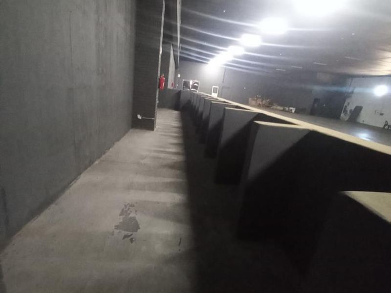 A large, open-plan industrial utility space featuring concrete flooring, dark-painted walls, and overhead recessed lighting, suitable for various commercial or storage applications.