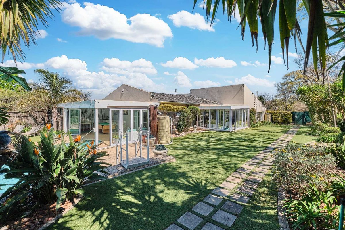 Rear view of the property featuring an enclosed patio, swimming pool, and a well-maintained garden with paved pathways.