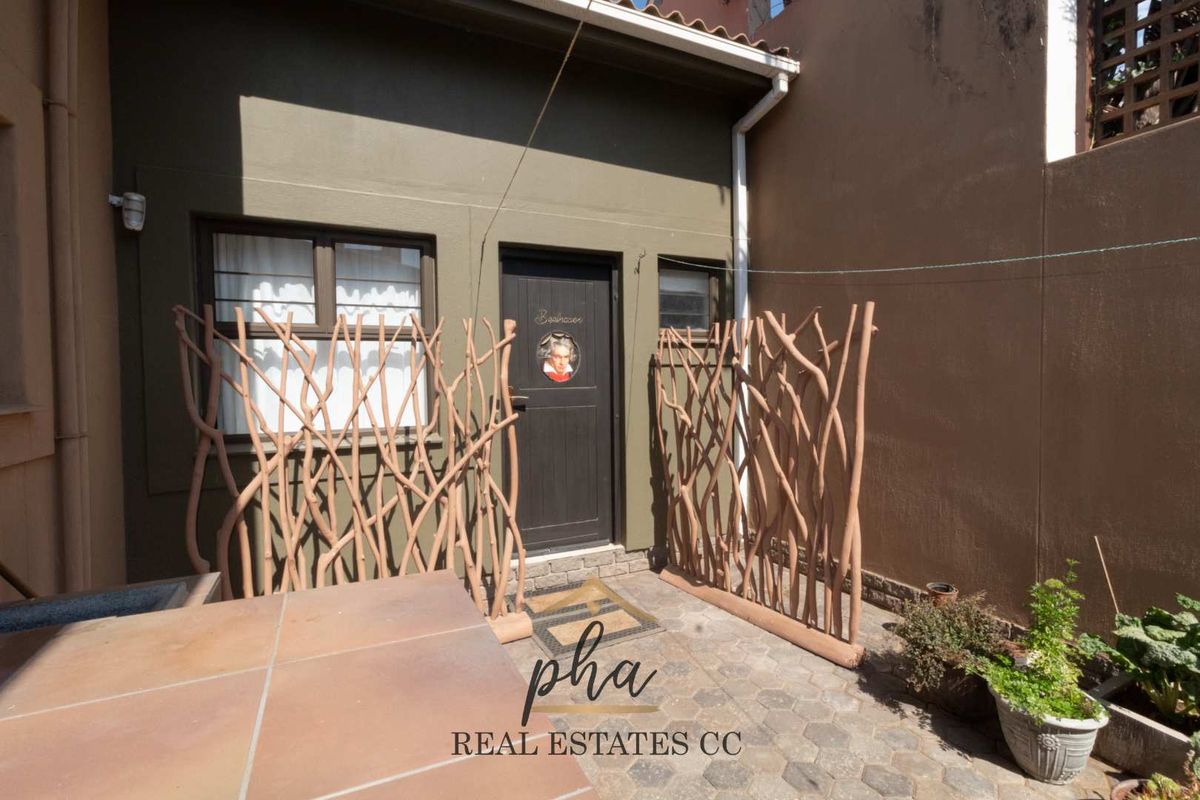 A rear exterior view of the property featuring a paved courtyard area, dark-toned exterior walls, and a private entrance door.