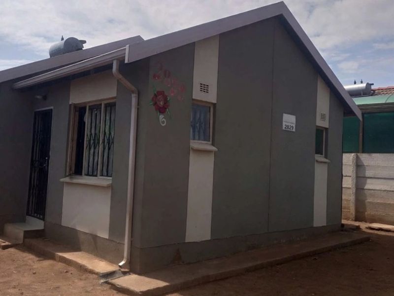 A single-story residential house featuring a painted exterior, solar water heating system, and security bars on windows.