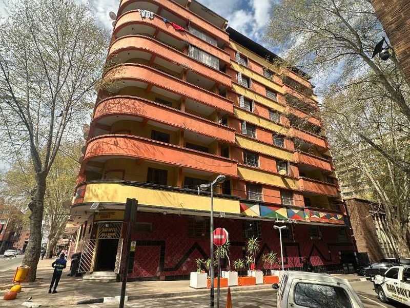 Street-level view of a multi-story apartment building featuring a distinctive curved facade with balconies and ground-floor commercial space.