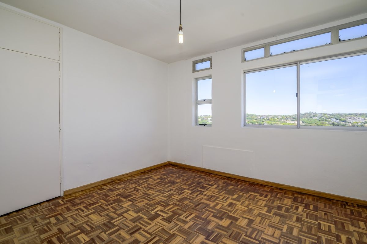 An empty bedroom featuring classic parquet flooring, built-in cupboards, and large windows offering natural light and elevated views.