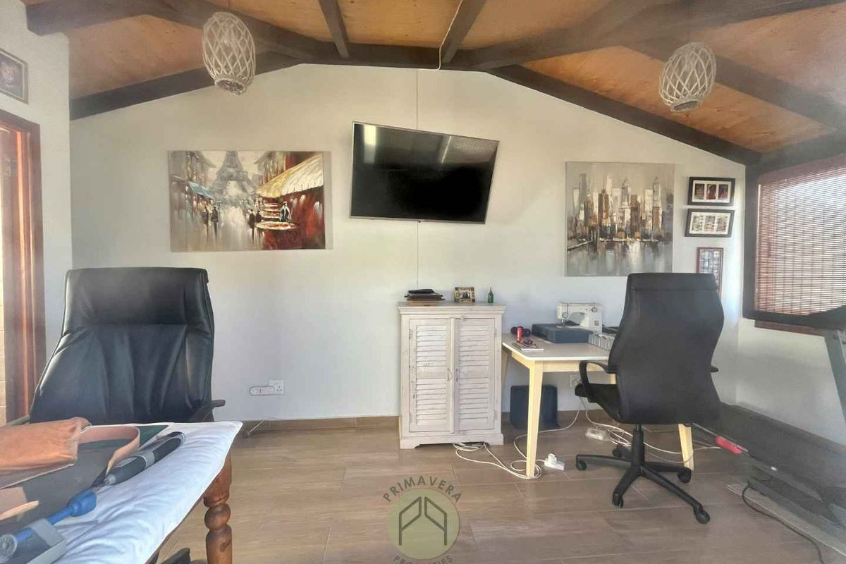 A versatile room featuring exposed timber ceiling beams, wood-look flooring, and a wall-mounted television, suitable for use as a home office or living space.