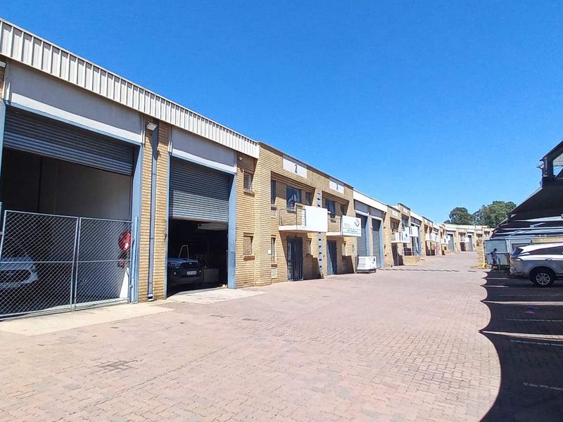 Industrial complex featuring multiple units with roller shutter doors, face brick exterior, and paved driveway with covered parking bays.