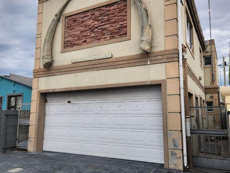 Front elevation of a multi-story property featuring a sectional garage door, paved driveway, and unique decorative exterior wall elements.
