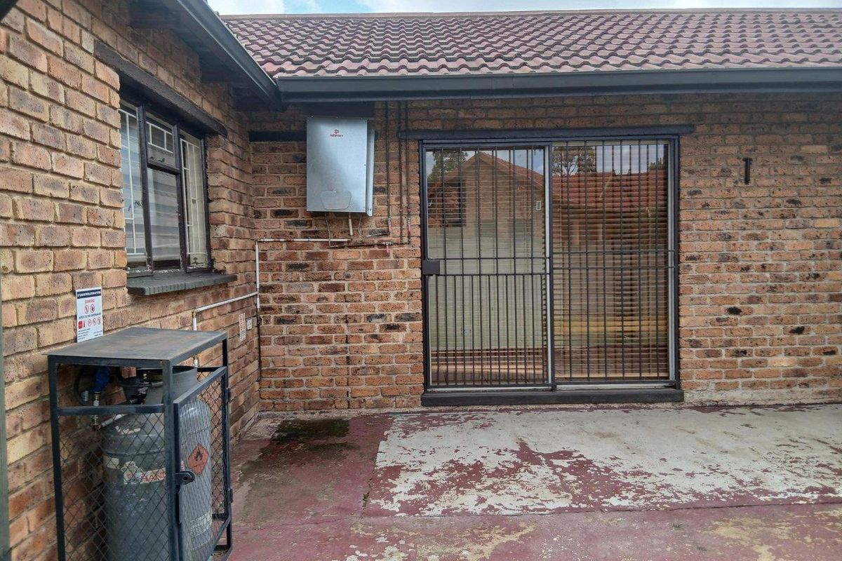 Rear exterior view of a brick house featuring a sliding door with security gate, gas geyser, and a concrete patio area requiring maintenance.