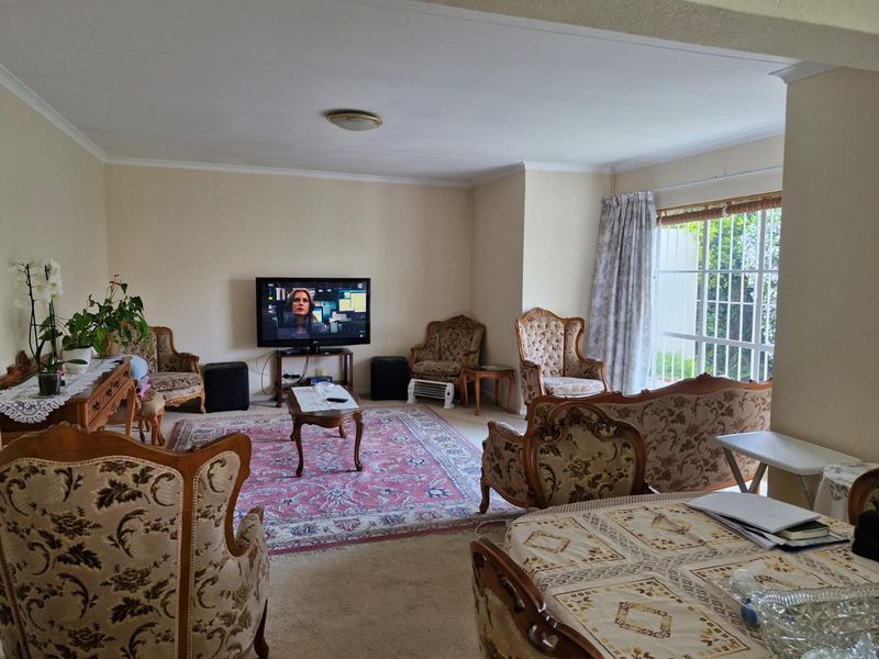 A spacious living room featuring carpeted flooring, a ceiling light fixture, and a sliding glass door with a security gate leading to the exterior.