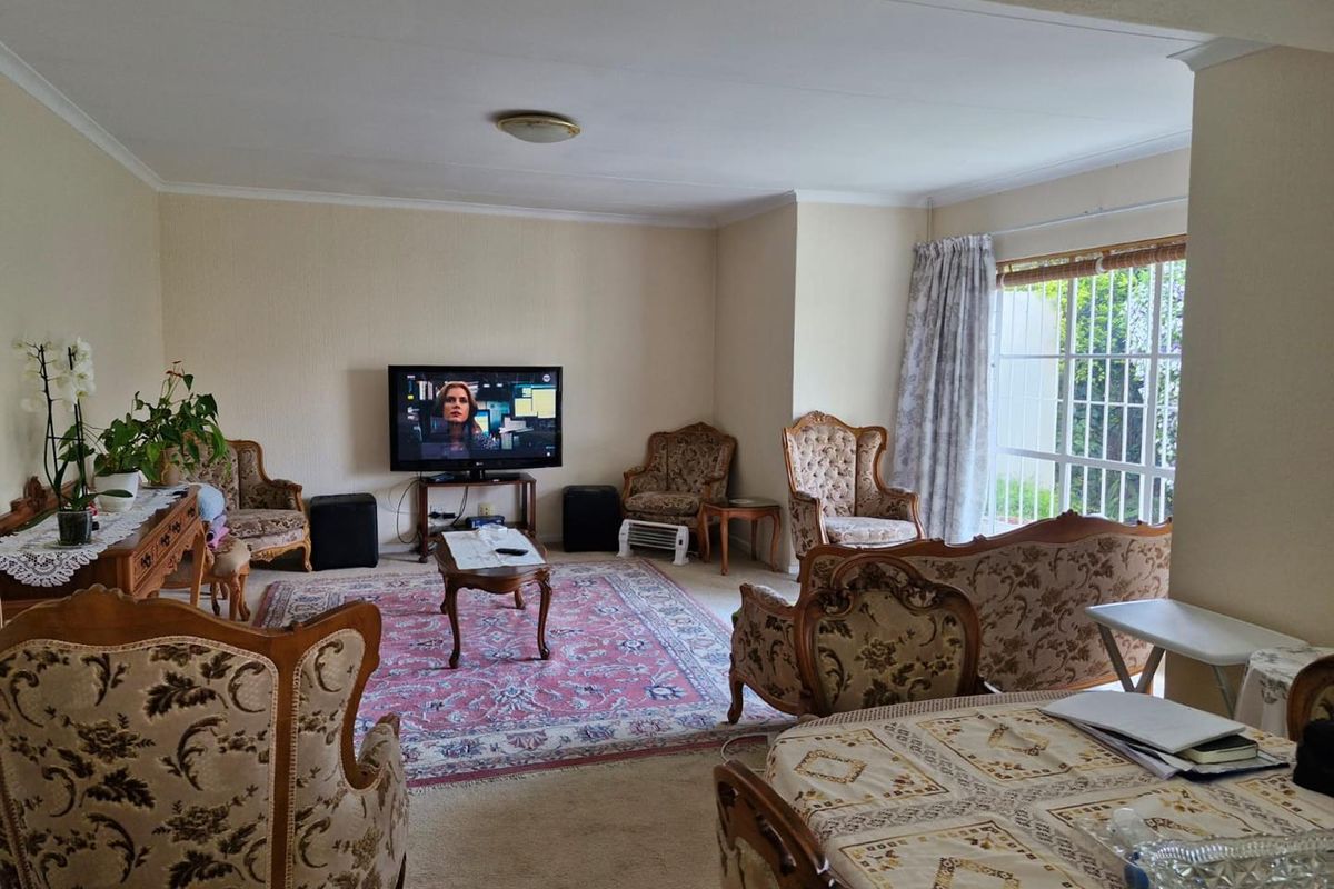 A spacious living room featuring carpeted flooring, a ceiling light fixture, and a sliding glass door with a security gate leading to the exterior.