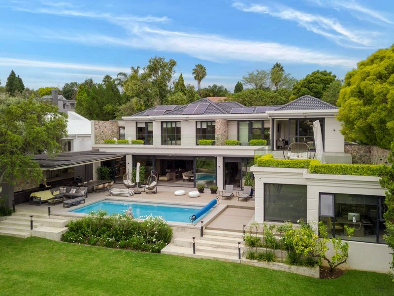 Stunning rear elevation featuring a modern swimming pool, expansive decking, covered patio area, and lush landscaped gardens with solar panels on the roof.