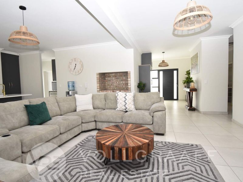 Spacious open-plan living area featuring tiled floors, an exposed brick fireplace, and modern pendant lighting, seamlessly connecting to the kitchen and entrance.