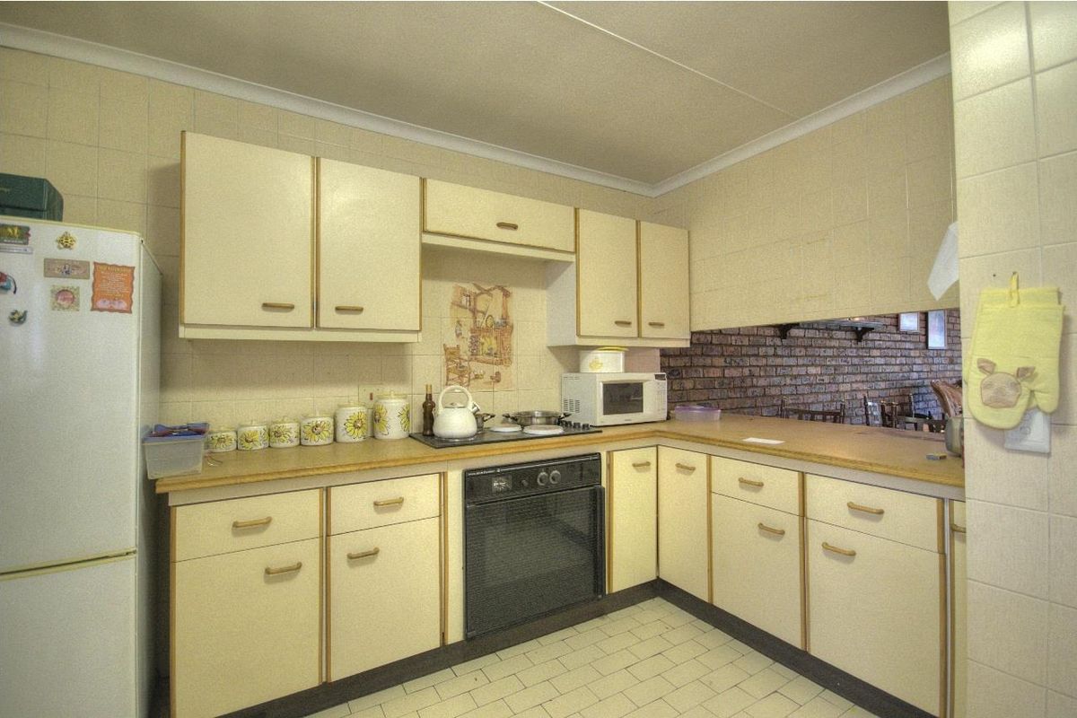A dated kitchen featuring laminate countertops, built-in oven, hob, and tiled walls, offering a functional layout with potential for modernization.