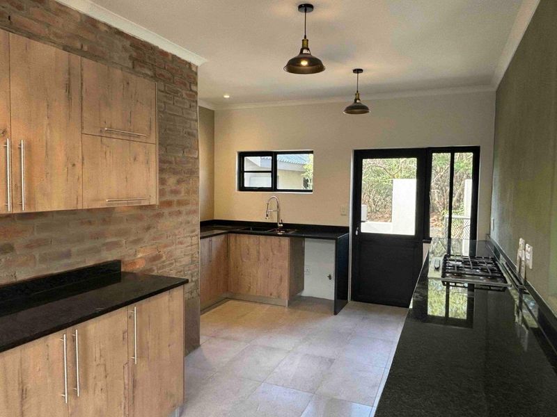 Modern kitchen featuring wood-finish cabinetry, granite countertops, a gas hob, and an exposed brick feature wall with direct access to the exterior.