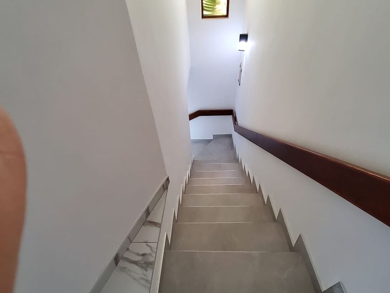 A staircase featuring tiled steps and a wooden handrail, leading down to a lower level.