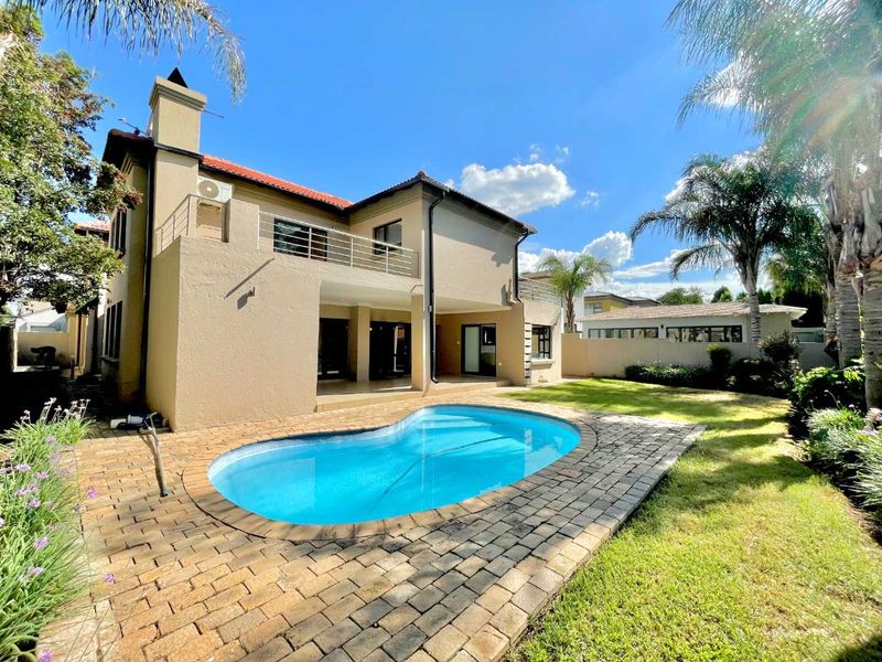 Rear view of the house featuring a swimming pool, paved pool deck, covered patio, and an upper-level balcony with a metal balustrade.