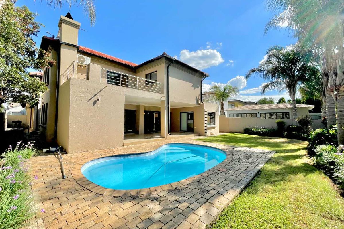 Rear view of the house featuring a swimming pool, paved pool deck, covered patio, and an upper-level balcony with a metal balustrade.