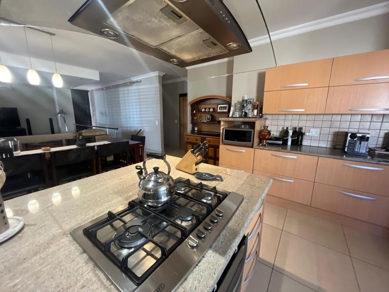 Open-plan kitchen featuring a central island with gas hob, granite countertops, and light wood cabinetry, flowing into the adjacent living and dining area.