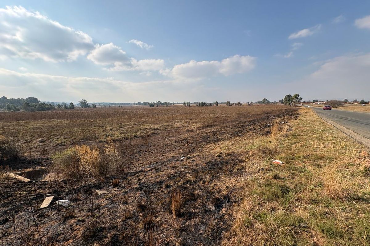 A wide-angle view of a vacant agricultural land parcel adjacent to a paved road, featuring open fields and natural landscape.