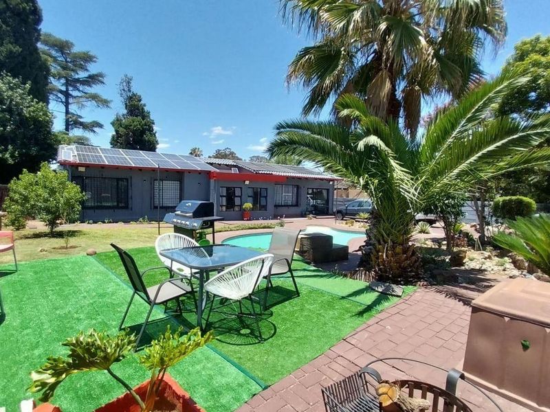 Spacious rear garden featuring a swimming pool, paved patio area, artificial lawn, and solar panels installed on the main house roof.