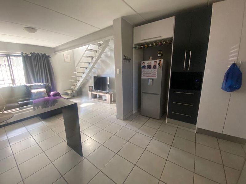 Open-plan living area featuring tiled flooring, built-in kitchen cabinetry, and a staircase leading to the upper level.