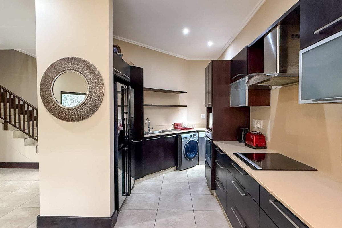 Modern kitchen featuring dark cabinetry, integrated appliances, sleek countertops, and a dedicated laundry area, seamlessly connected to the staircase and living space.
