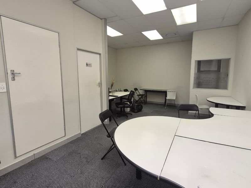 A functional office space featuring carpeted flooring, recessed ceiling lighting, and an internal window, suitable for a professional work environment.