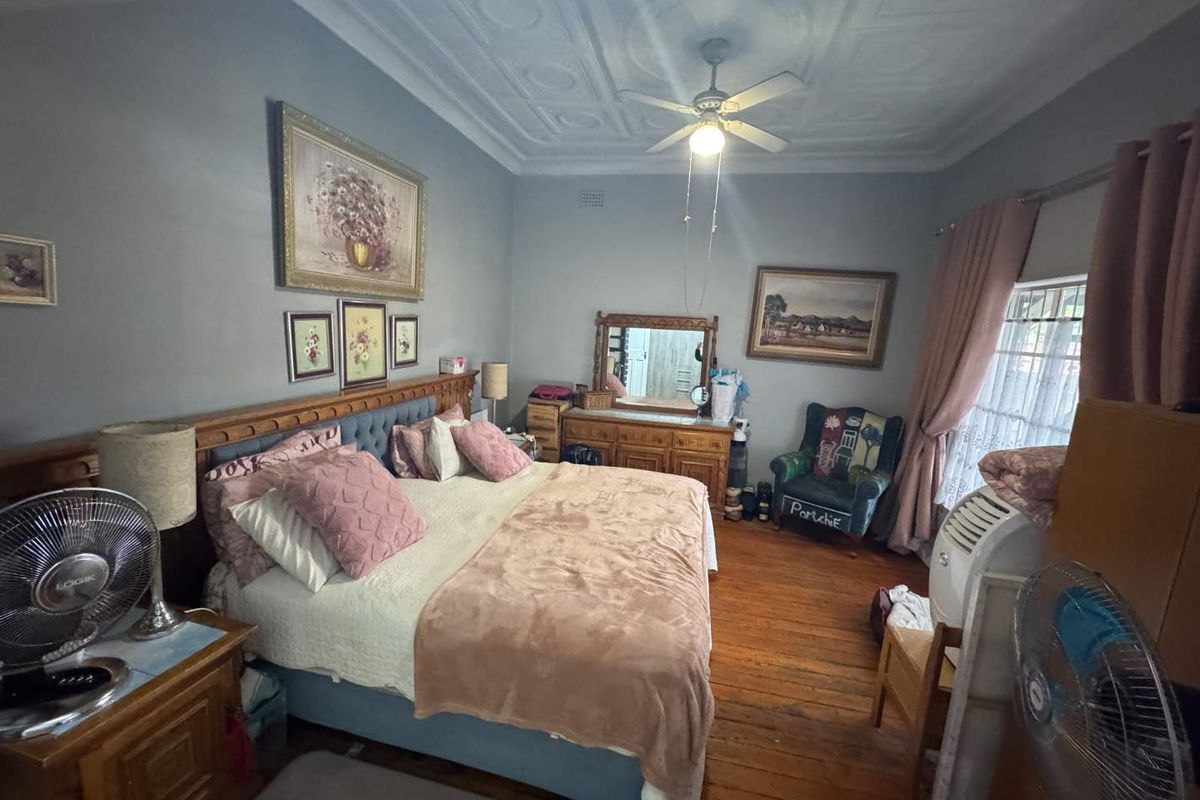 Spacious bedroom featuring original timber flooring, decorative pressed metal ceiling, and a ceiling fan.