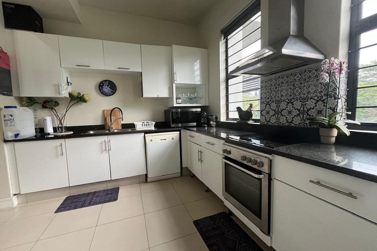 Modern kitchen featuring white cabinetry, dark granite countertops, a stainless steel oven with extractor fan, and decorative patterned backsplash tiling.