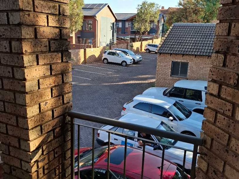 A view from a balcony featuring brick pillars and a metal balustrade, overlooking a paved parking area within the townhouse complex.