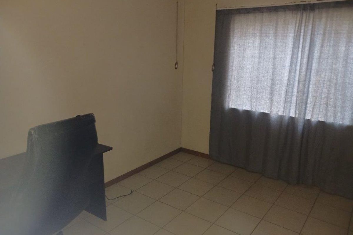 A sparsely furnished bedroom featuring tiled flooring and a window with curtain tracks, requiring minor cosmetic updates to improve its overall appeal.