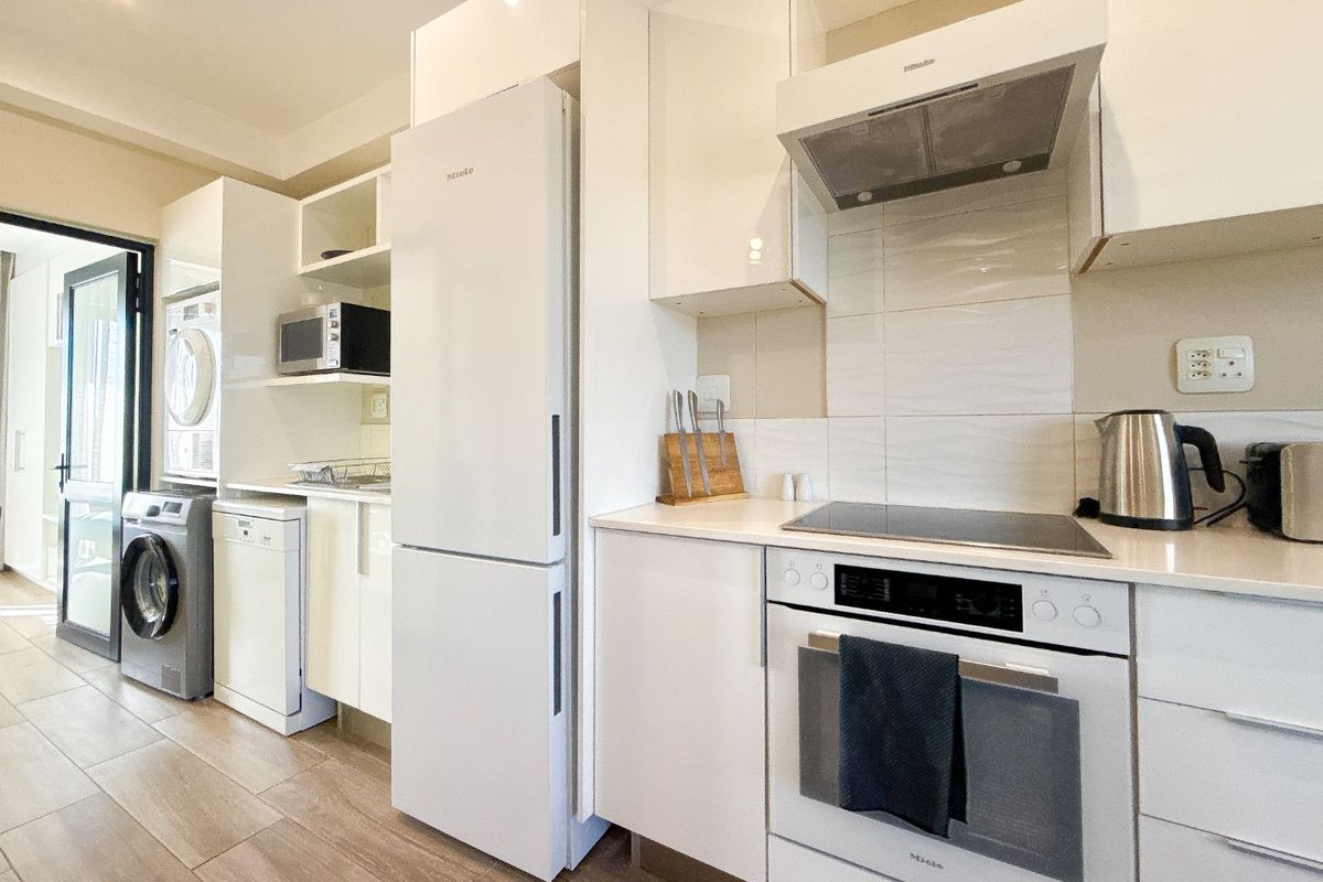 Modern kitchen featuring high-gloss white cabinetry, integrated Miele appliances, electric cooktop, extractor fan, and durable tiled flooring with direct access to an outdoor area.