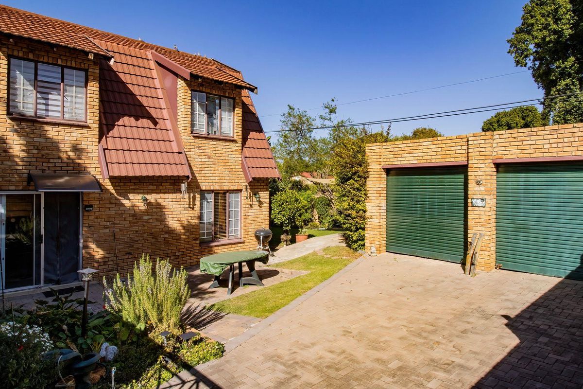 Rear view of a face brick townhouse featuring a tiled roof, paved driveway, double garage, and a private garden area.