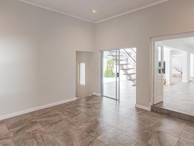 A bright, empty living area featuring neutral tiled flooring, a modern staircase, and seamless access to an outdoor space through a sliding glass door.