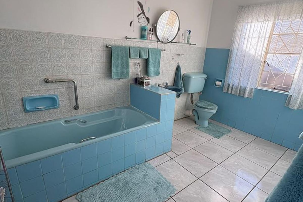 A dated bathroom featuring blue sanitaryware, ceramic wall and floor tiling, and a wall-mounted heater.