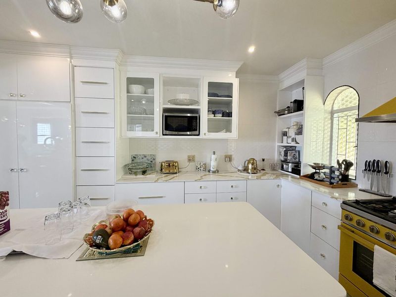 A bright, modern kitchen featuring white cabinetry, stone countertops, a central island, and a distinctive yellow gas stove.