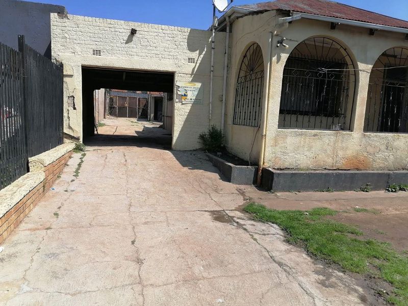 Front exterior view of a property featuring a concrete driveway, covered carport area, and an arched veranda with security bars.