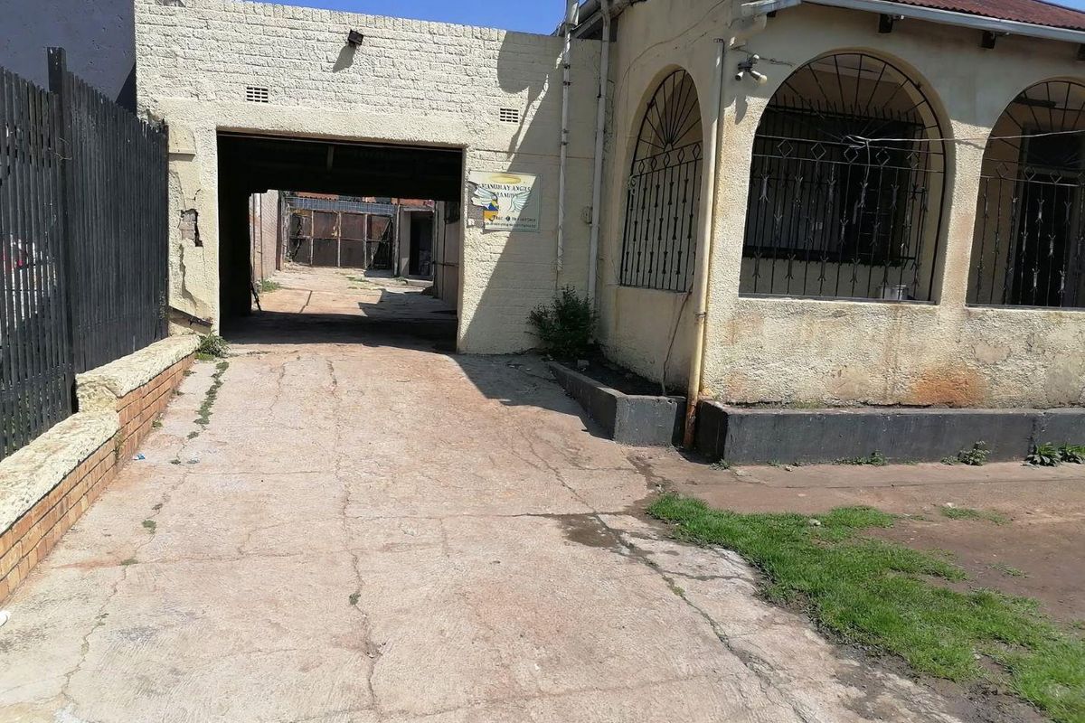 Front exterior view of a property featuring a concrete driveway, covered carport area, and an arched veranda with security bars.