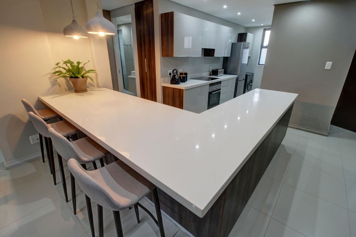 Modern kitchen featuring a large L-shaped quartz breakfast bar, sleek built-in cabinetry, integrated appliances, and contemporary recessed and pendant lighting.