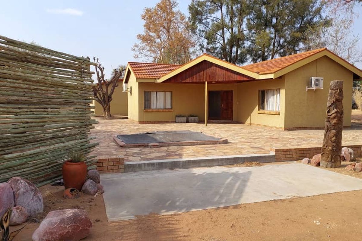 A single-story farm dwelling featuring a paved patio area, tiled roof, and rustic wooden privacy screening in a rural setting.