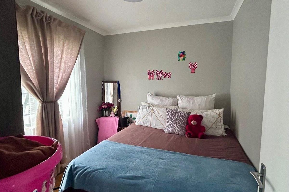A compact bedroom featuring neutral wall paint, a ceiling light fixture, and a window with installed curtain rods.