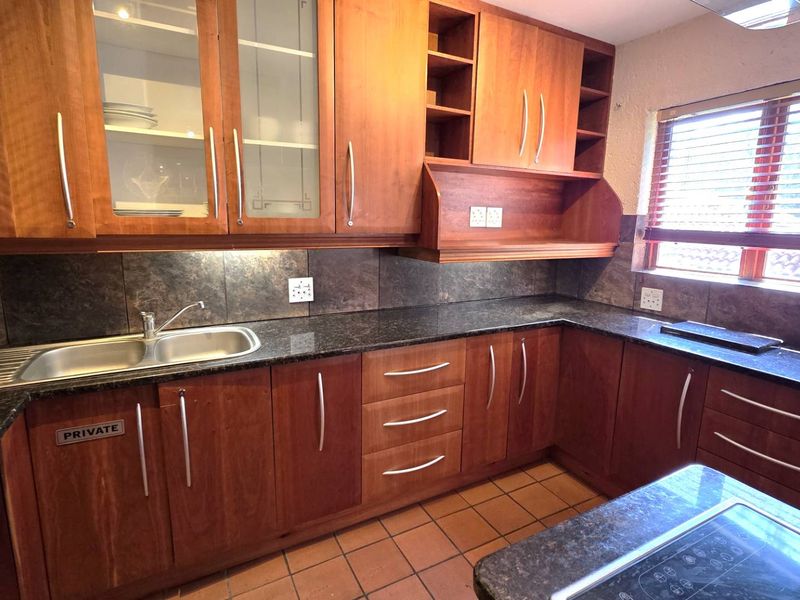 A functional kitchen featuring warm-toned wooden cabinetry, dark granite countertops, a double bowl sink, and tiled flooring with ample storage space.