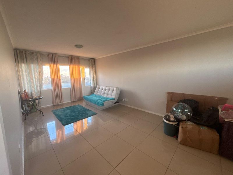 A spacious living area featuring large windows, neutral tiled flooring, and ample natural light, providing a versatile space for comfortable living.