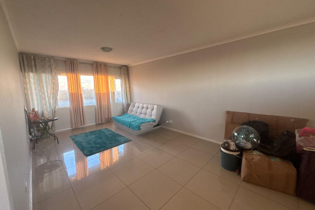 A spacious living area featuring large windows, neutral tiled flooring, and ample natural light, providing a versatile space for comfortable living.