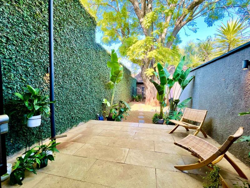A private outdoor patio area featuring stone paving, a lush ivy-covered boundary wall, and a landscaped garden path leading to a large mature tree.