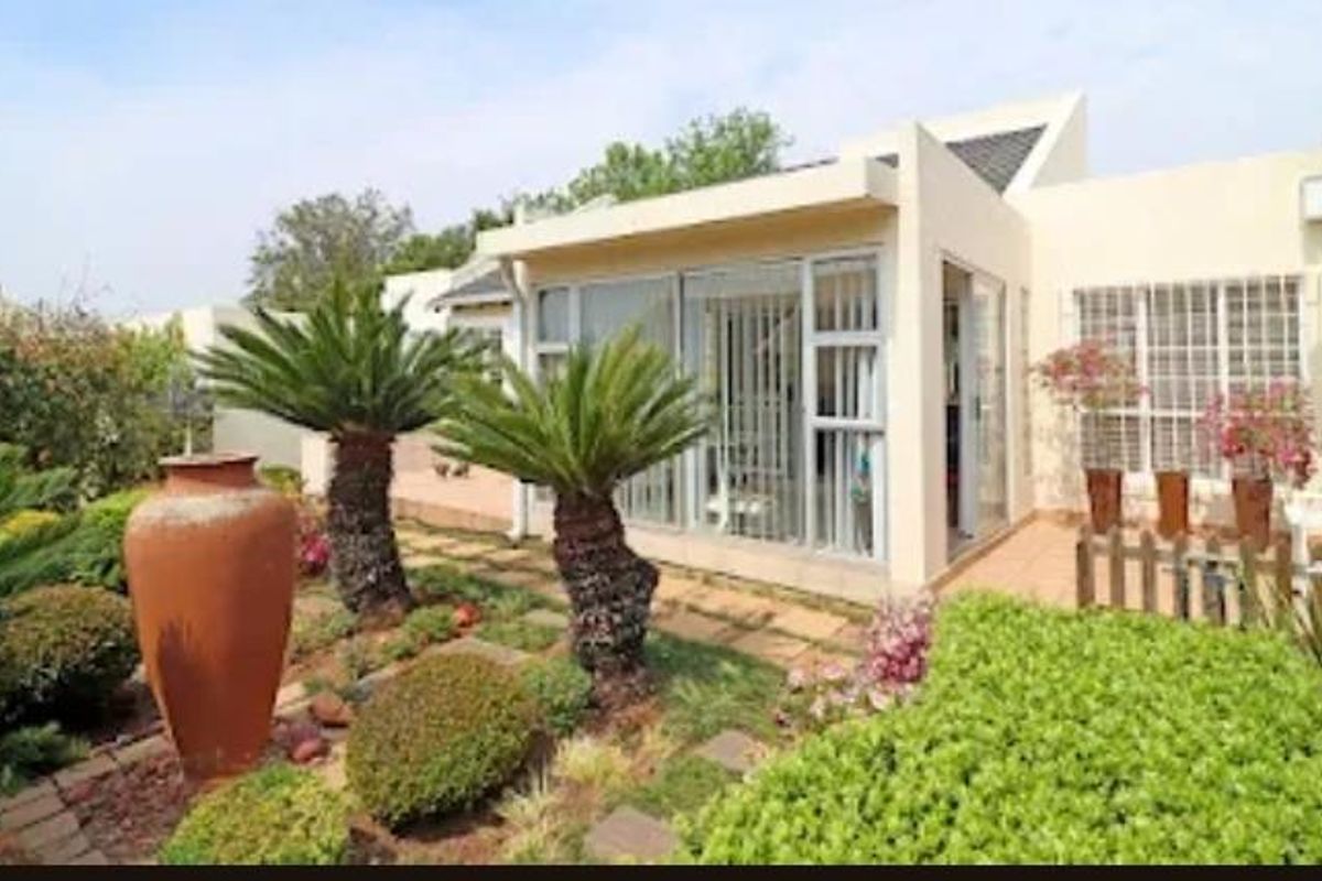 A well-maintained retirement village unit featuring a paved patio area, aluminium-framed windows, and established garden landscaping.